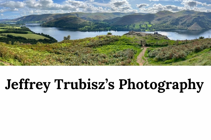 A wide landscape photograph of mountains and a body of water, by Jeffrey Trubisz